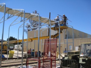 Restoration volunteers attach roofing panels to the carport frame